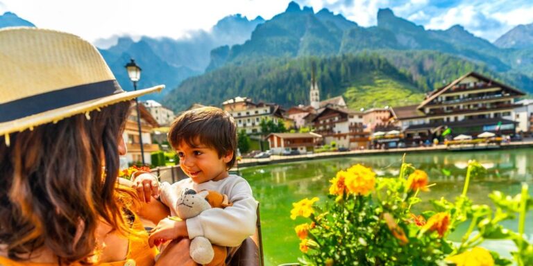 Mother holding her son enjoying the view of alleghe lake and civetta mountain range in the italian dolomites