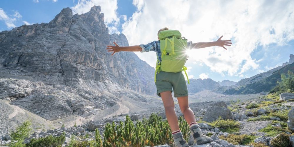 Young woman arms outstretched on top of rock in Alto Adige region, Italy.